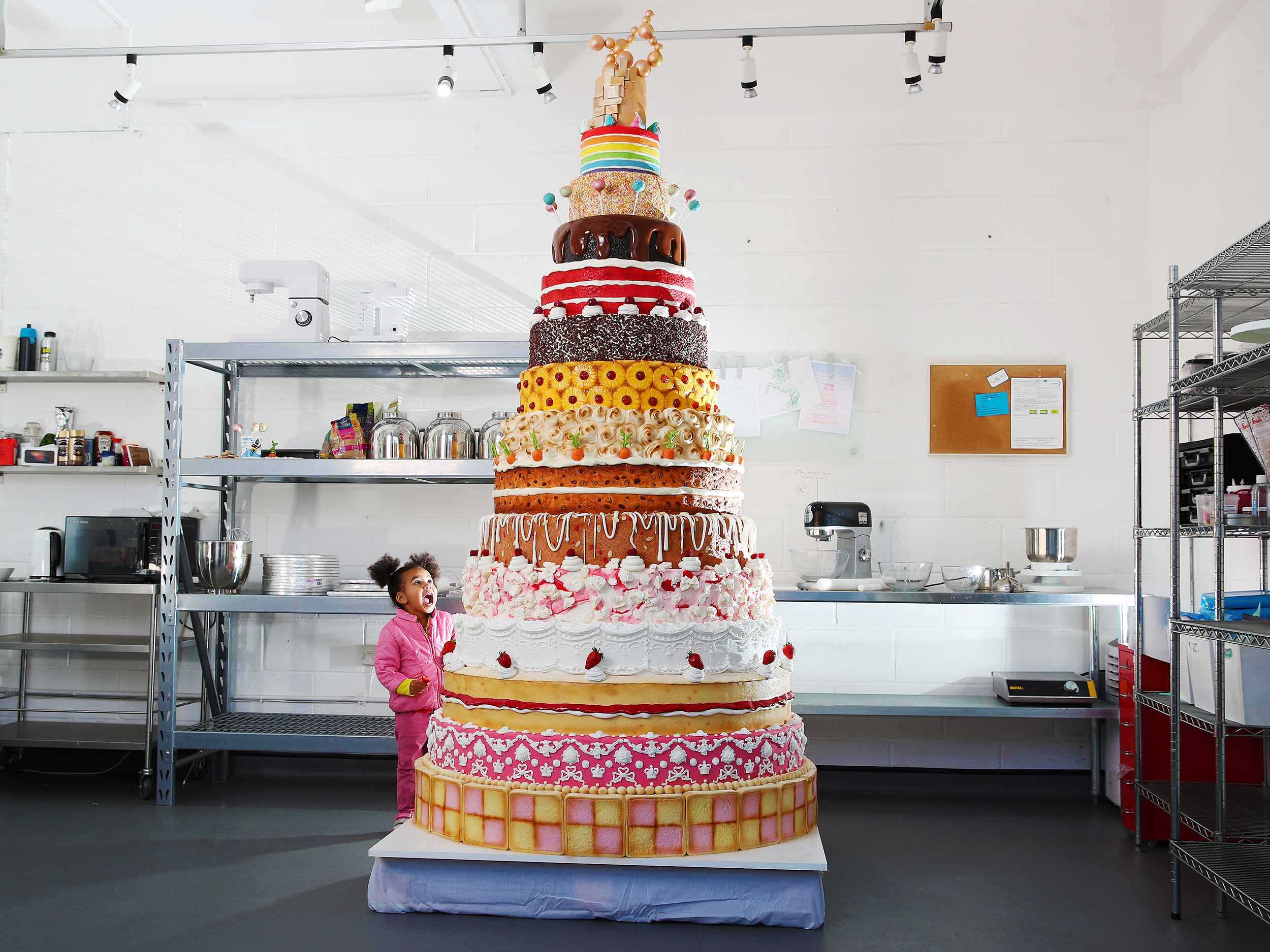 Giant cake with many layers and an astonished child looking up at it