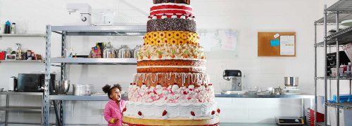 Giant cake with many layers and an astonished child looking up at it
