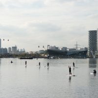 Seven people in wetsuits paddleboarding on the water at the Royal Docks
