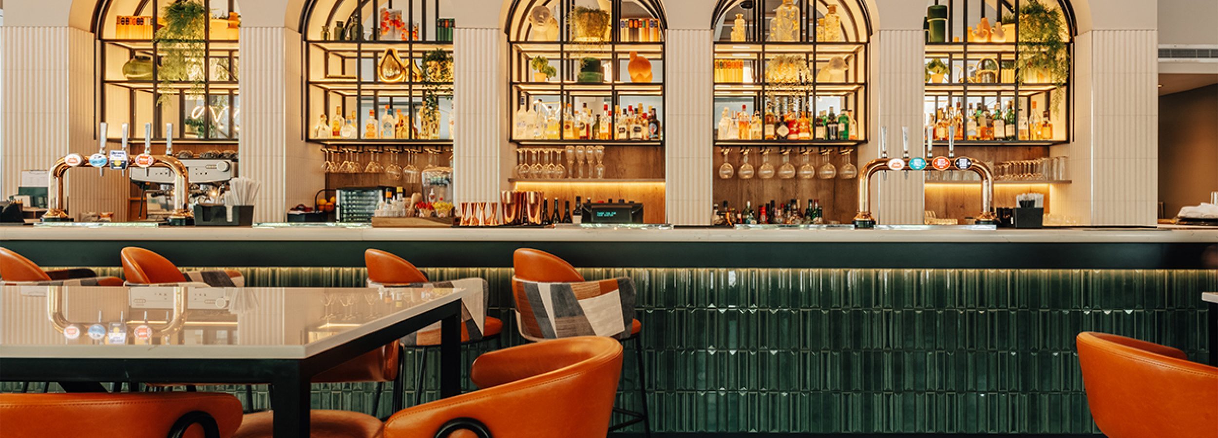 A photo of a neatly presented bar with orange chairs and stools