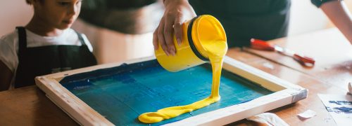 A yellow pot of paint being poured on a board