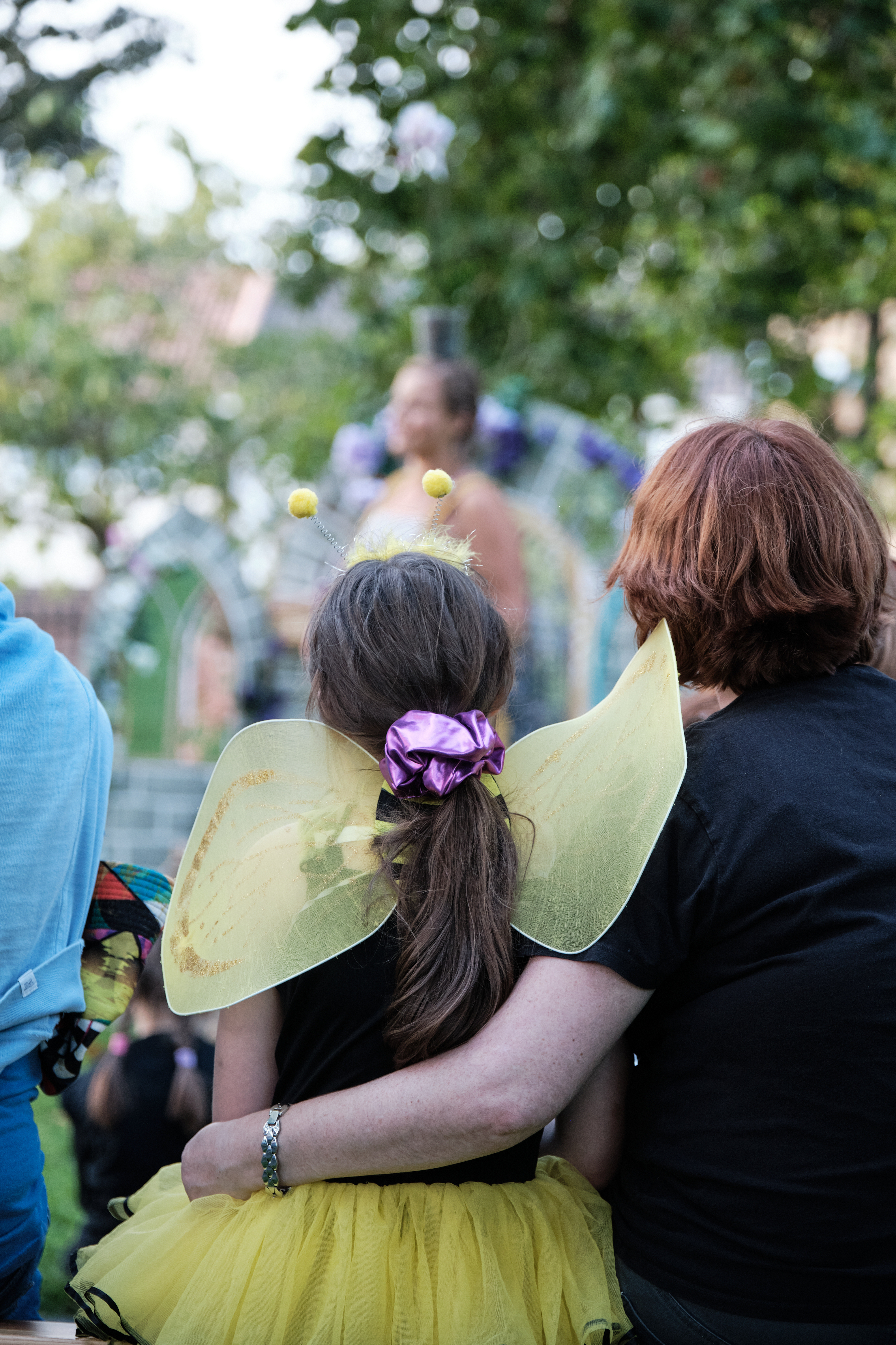 Girl in bee costume sits in audience with mother