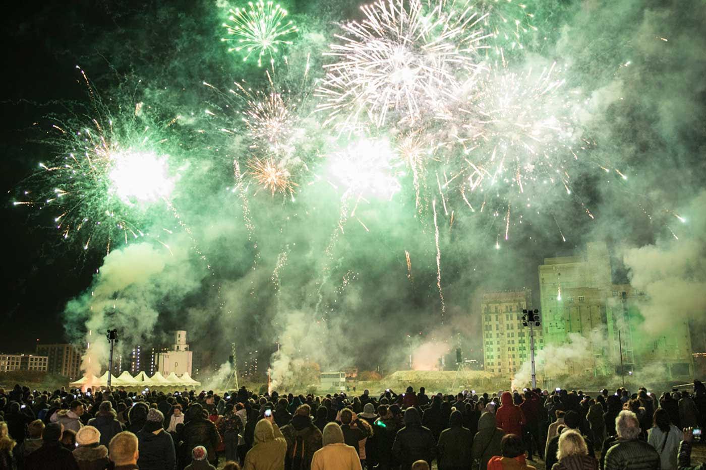 Night sky filled with green fireworks with a huge crowd looking up at them