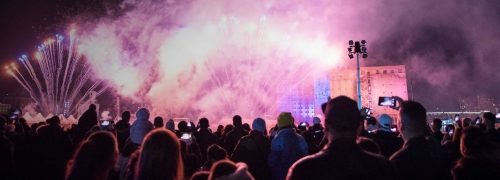 Night sky filled with pink fireworks with a huge crowd looking up at them