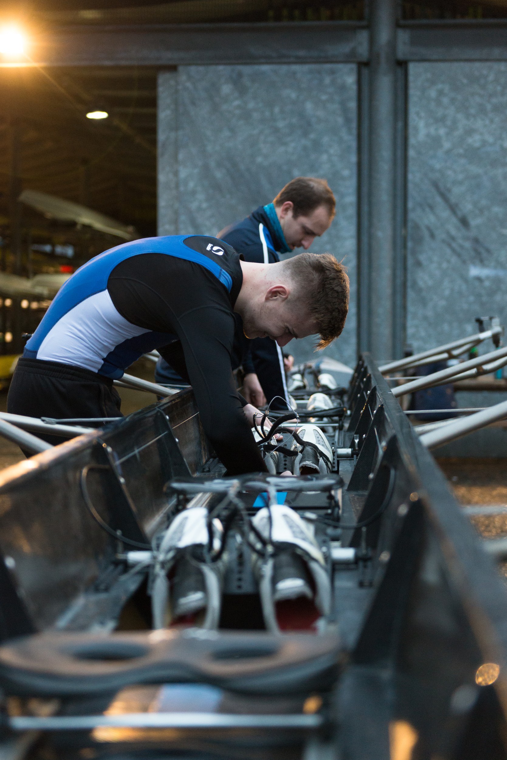 Two men preparing a rowing boat outside boat shed