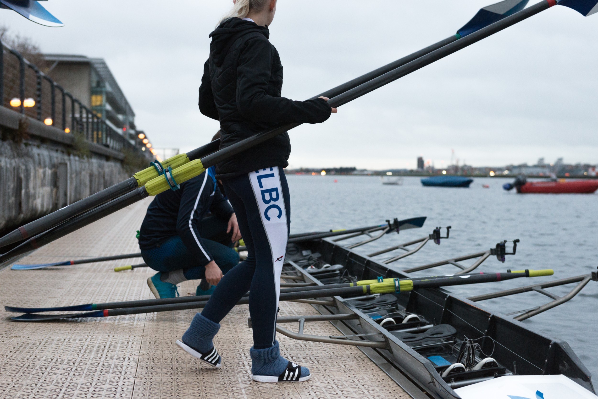 Two people on the edge of the water with a rowing boat and oars