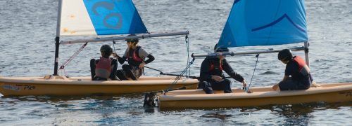 Two small sailing boats being sailed by two young people in each