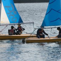 Two small sailing boats being sailed by two young people in each