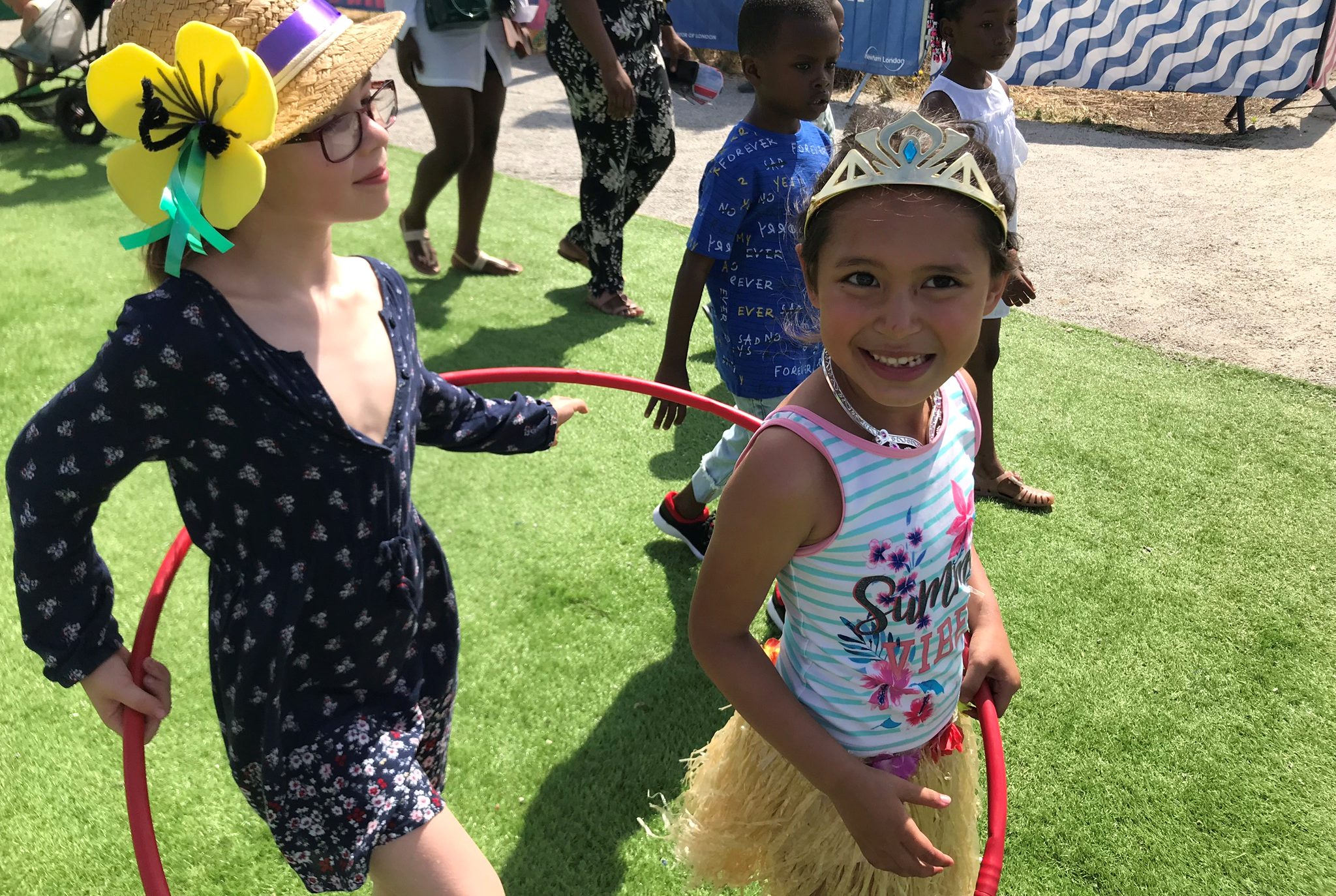 Two children playing with a red hula hoop on grass