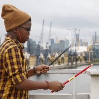 Child using drum sticks on railing at the Royal Docks