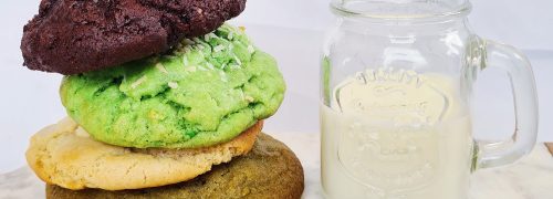 A stack of colourful cookies next to a glass of milk