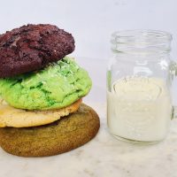A stack of colourful cookies next to a glass of milk