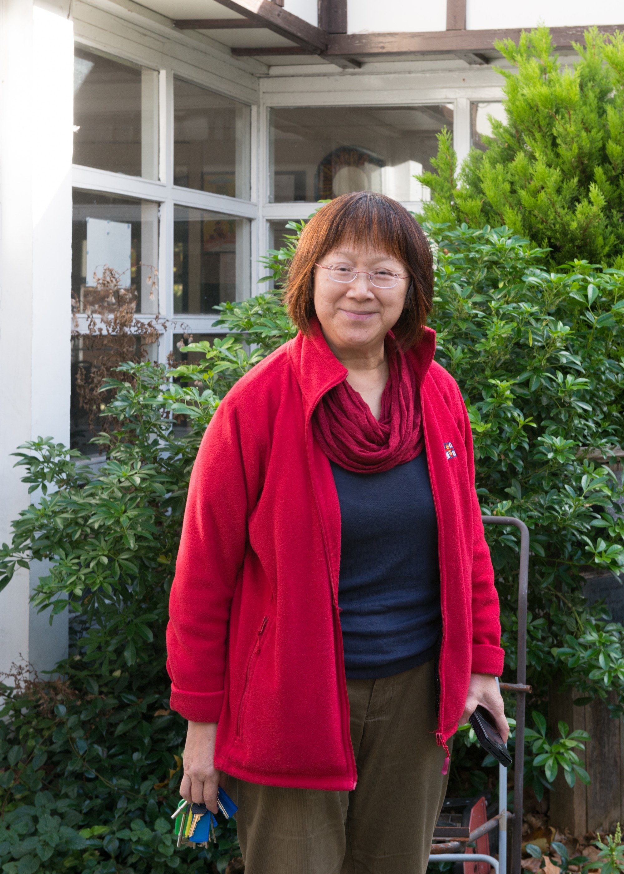 Portrait of Gill Tan, smiling slightly, outside with foliage in the background