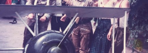 Group of men in unusual costumes standing behind a large model plane