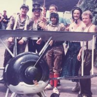 Group of men in unusual costumes standing behind a large model plane