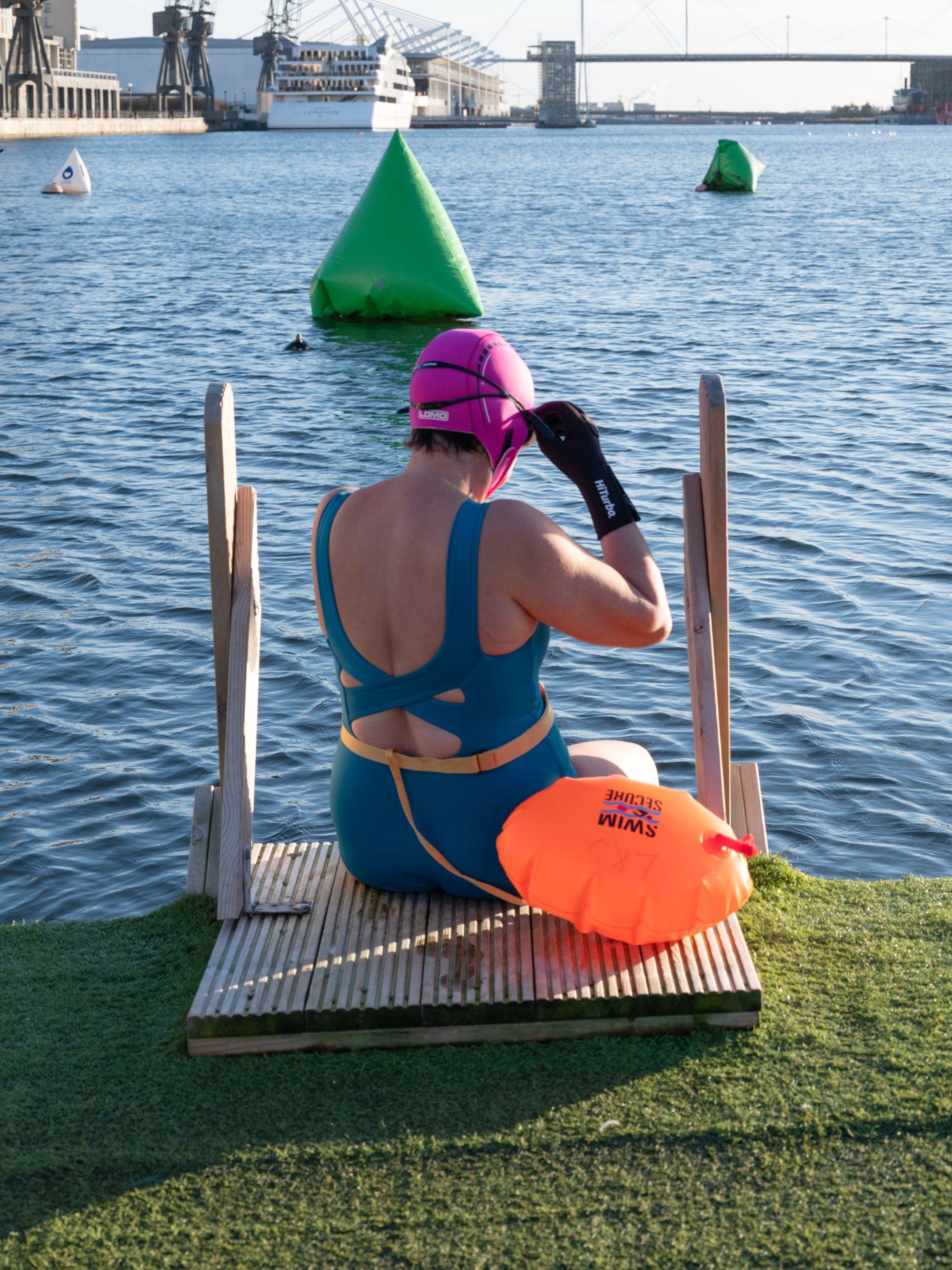 Swimmer in a bathing suit and cap sitting on the dock edge ready to go in