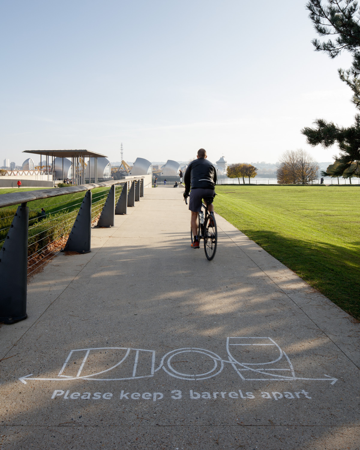 Man cycling past words that say "please keep 3 barrels apart"