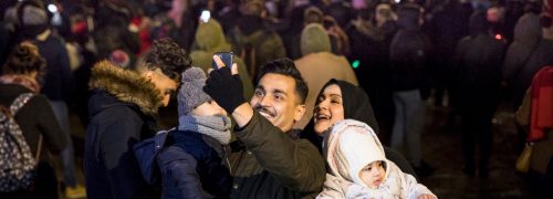 A couple with children taking a selfie in front of a large crowd