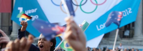 A young girl waves a flag in the crowd before the Olympic rings