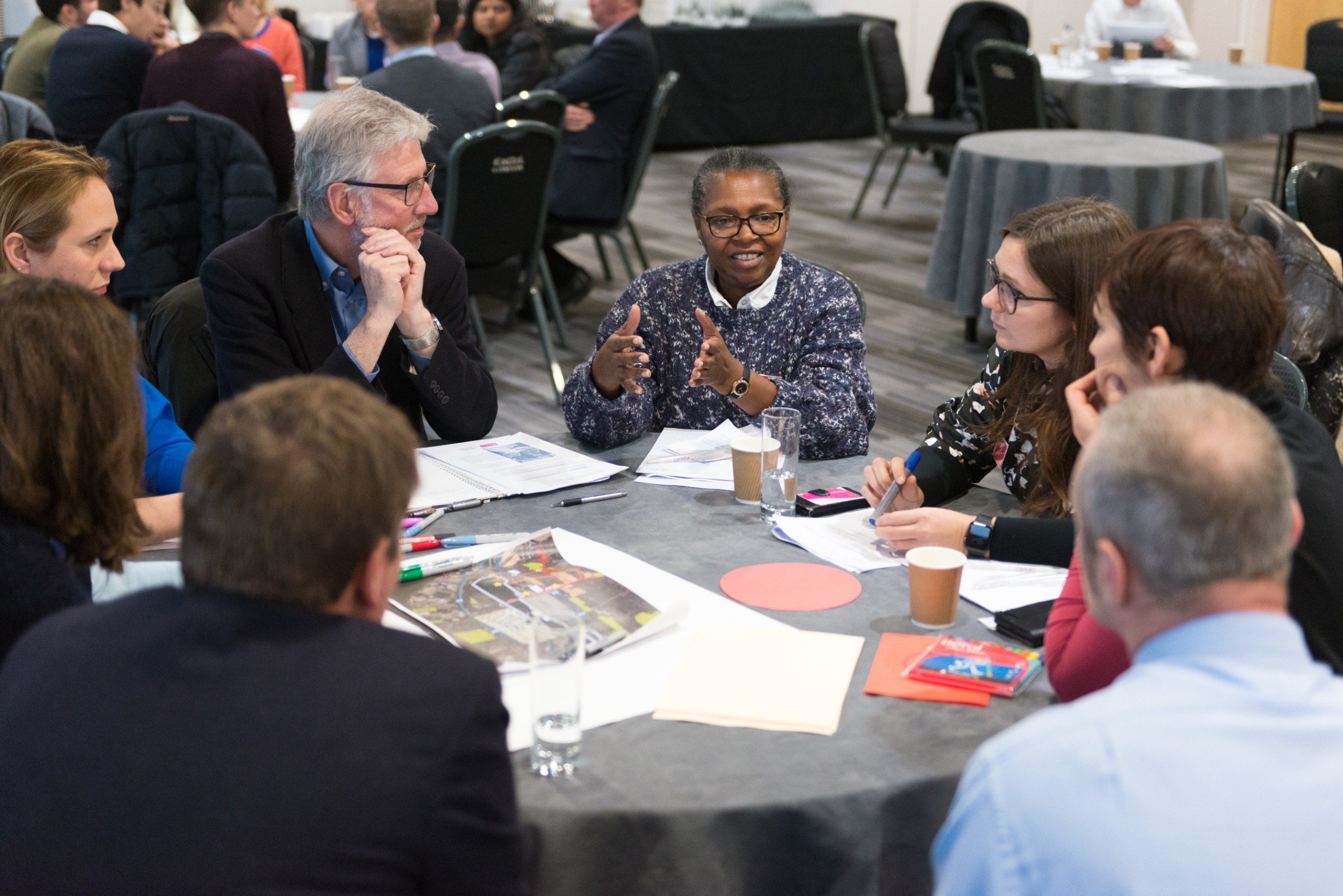 Group of people around a table with large pieces of paper, in discussion