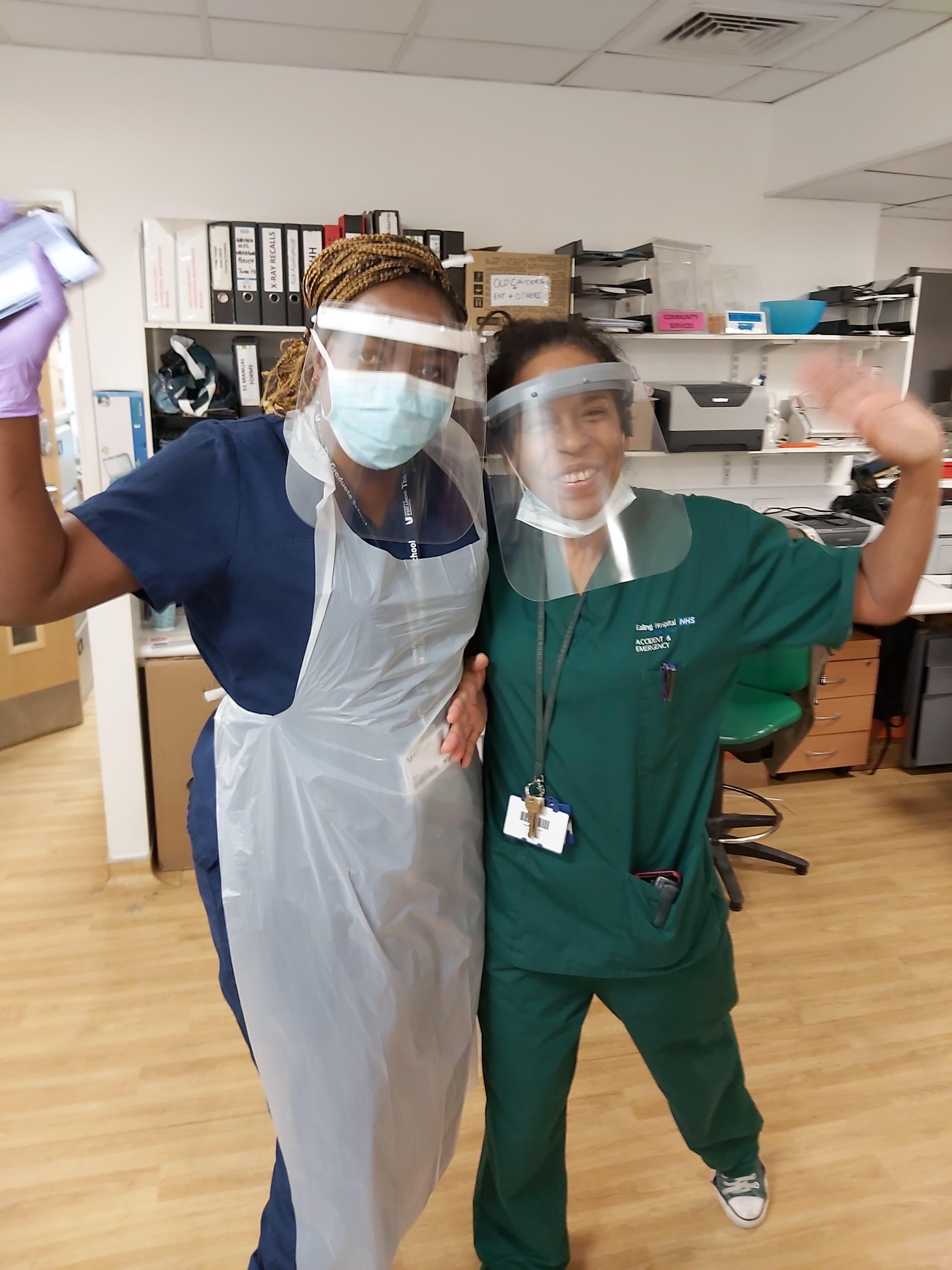 Two women in scrubs wearing plastic face visors and smiling