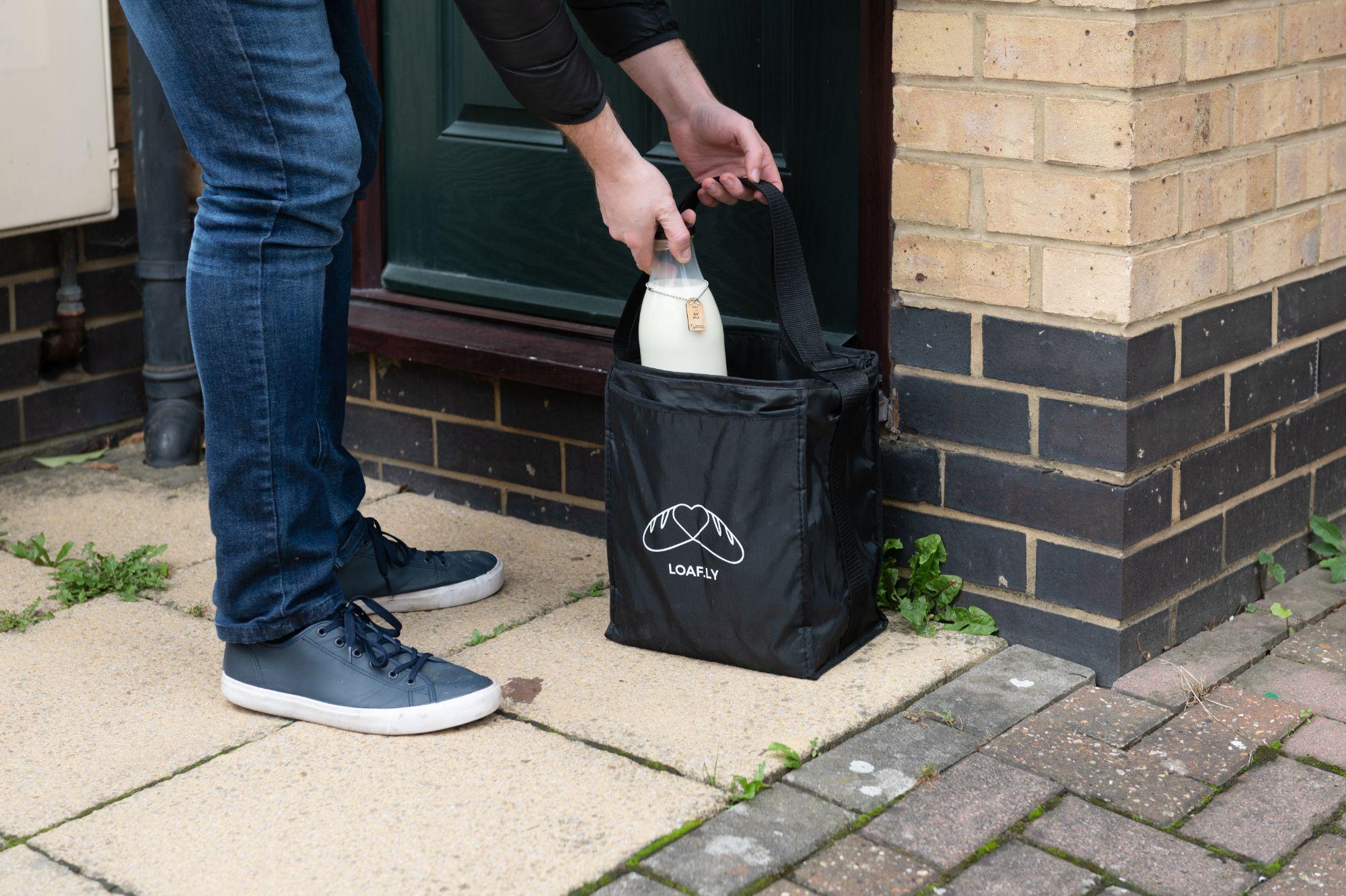 A bottle of milk being lowered into a loafly delivery bag