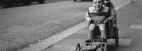 Black and white photo of two young boys go-karting on the street