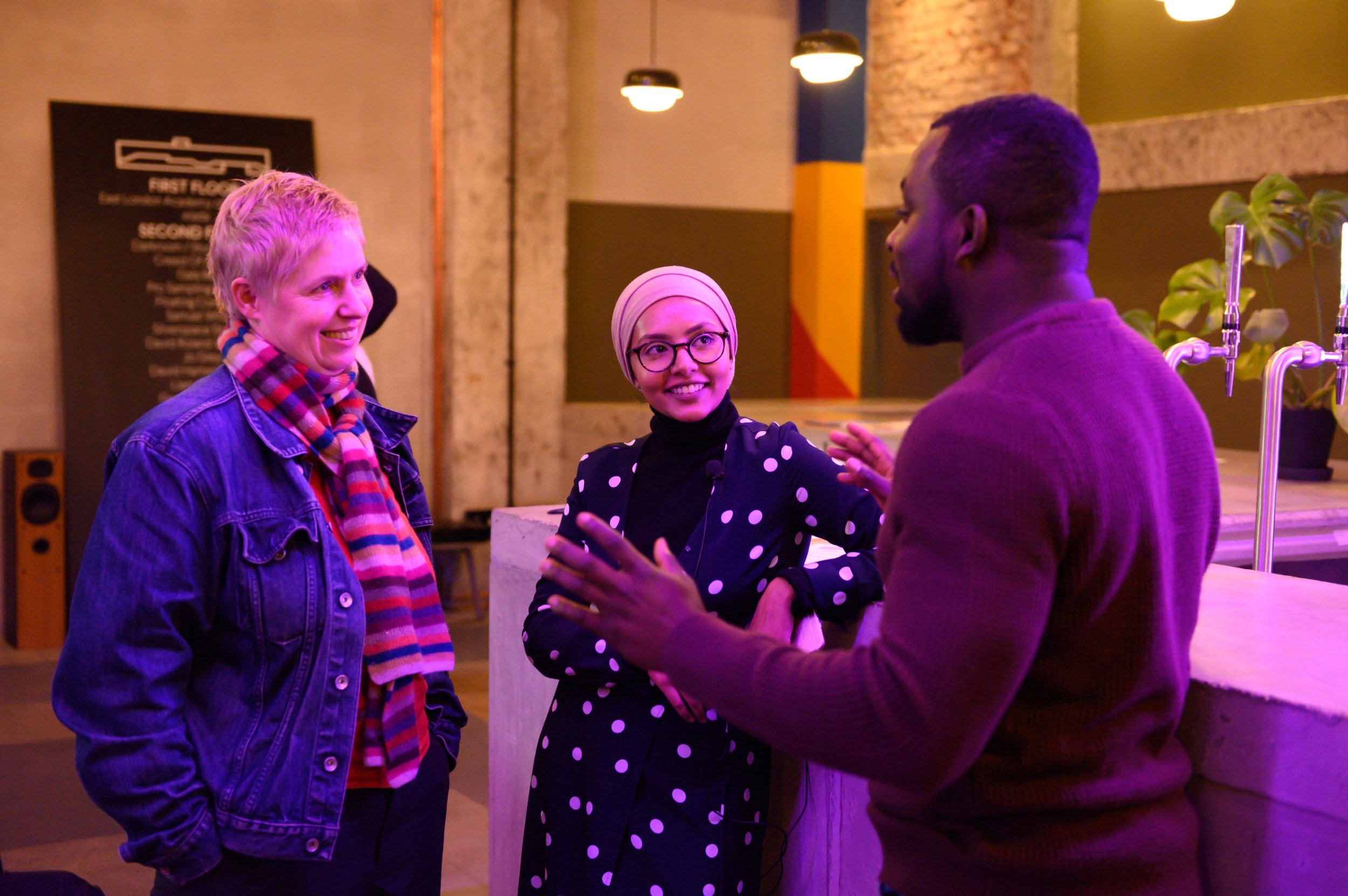 Three people smiling and chatting at a bar