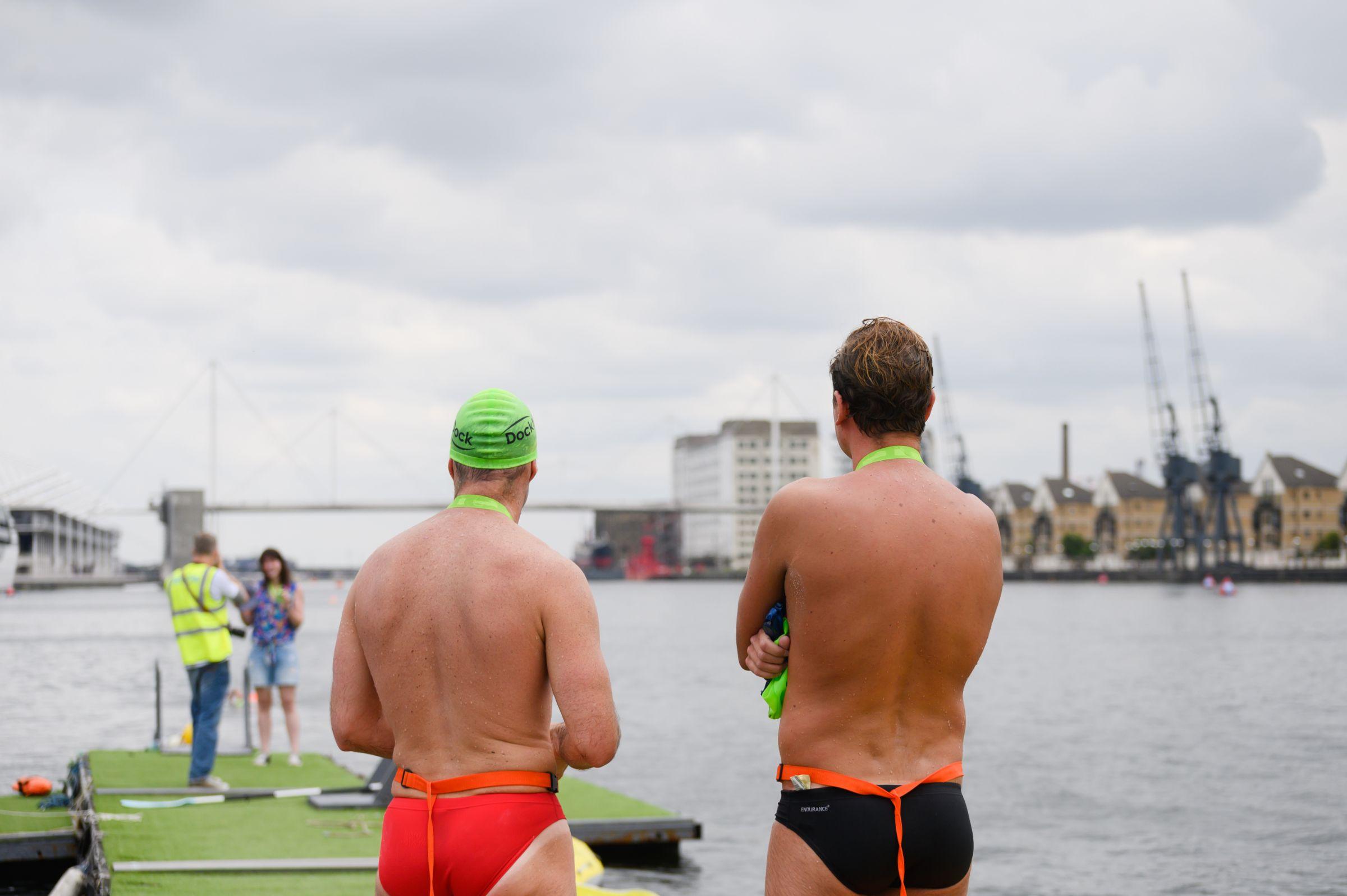 Two men in swimming costumes looking out on to the water at the Royal Docks