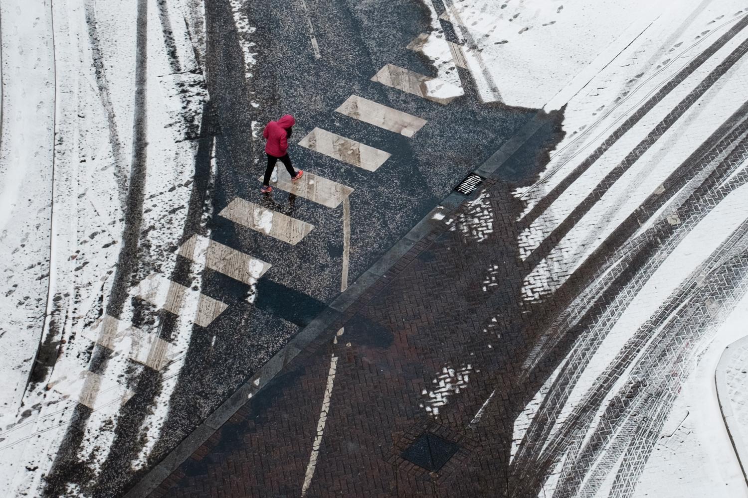 A man in a red coat crossing the road surrounded by snow