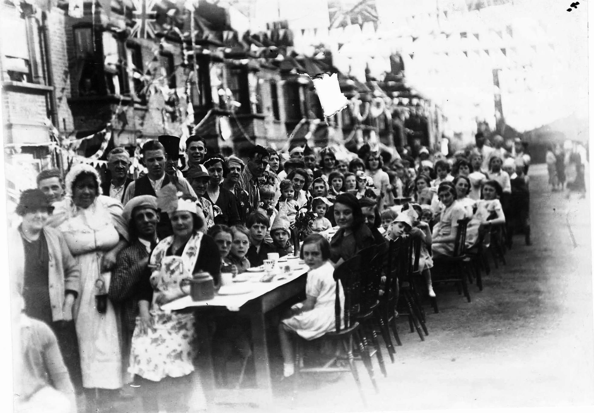festive scenes in the street for the 1935 jubilee, with people sat at a table in the street