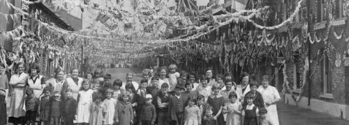Historic photo of a street party with lots of bunting over the crowd