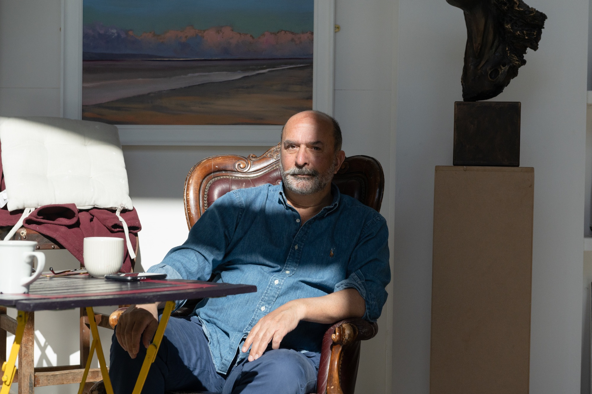 Portrait of a man sitting inside with paintings and sculpture around him