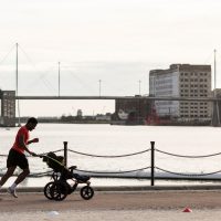 A runner jogging along the docks while pushing a pram