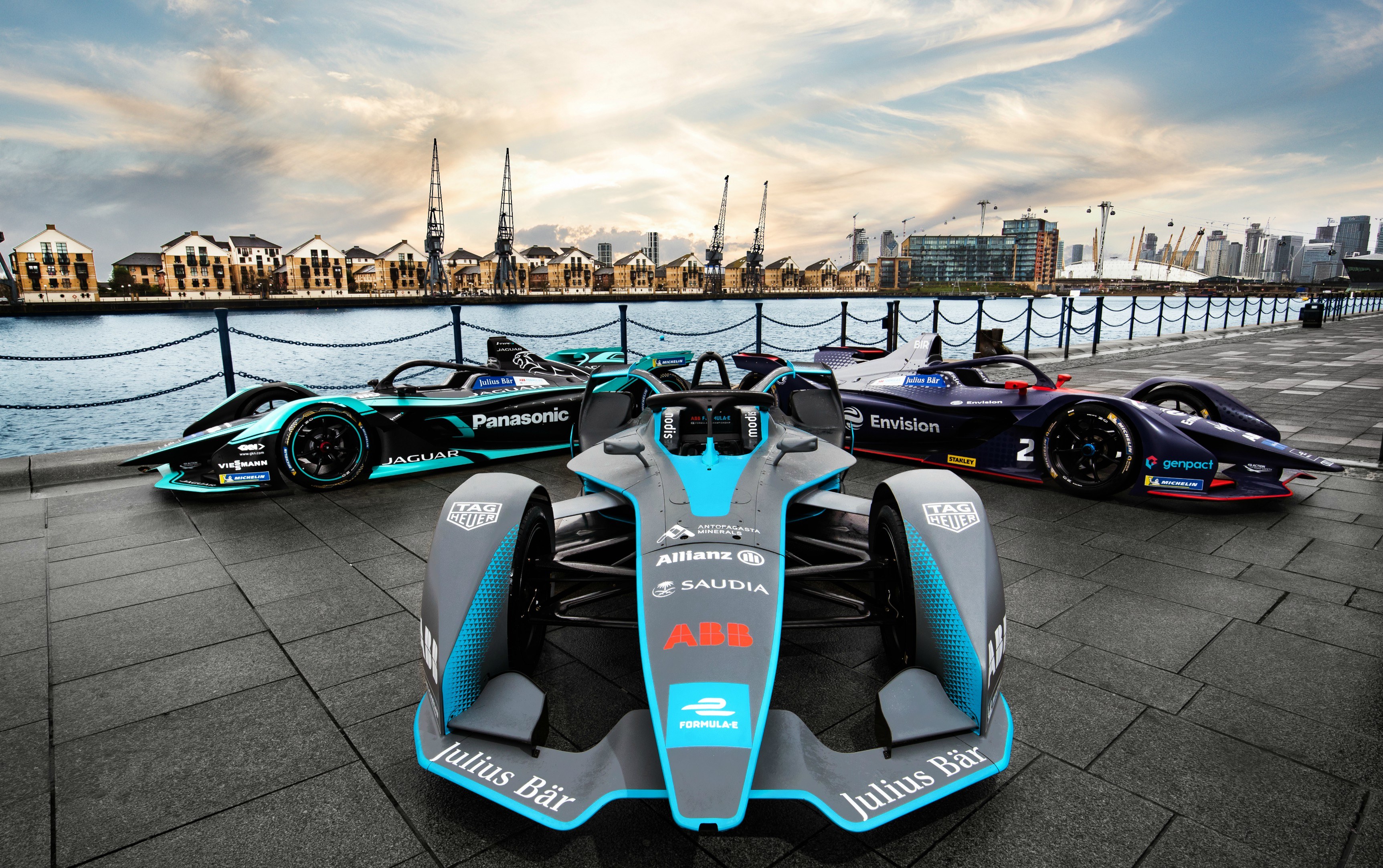 Three Formula E cars on display with the docks in the background