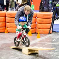 A man guides a small child riding a bike over a ramp