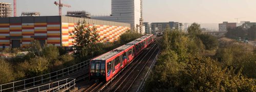 DLR train running between trees and building